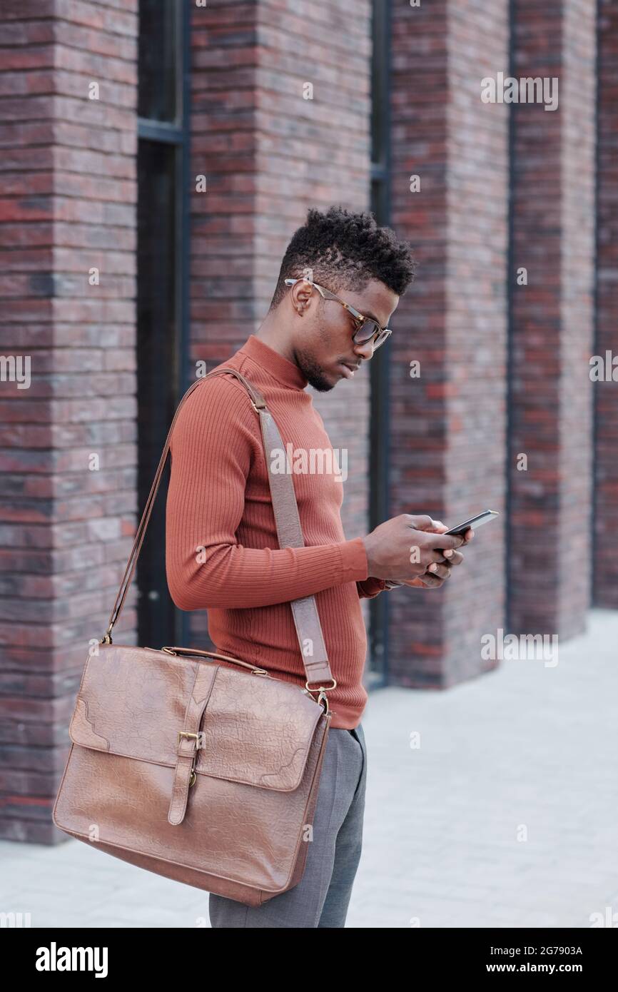 Uomo d'affari africano con borsetta sullo scorrimento delle spalle in smartphone Foto Stock
