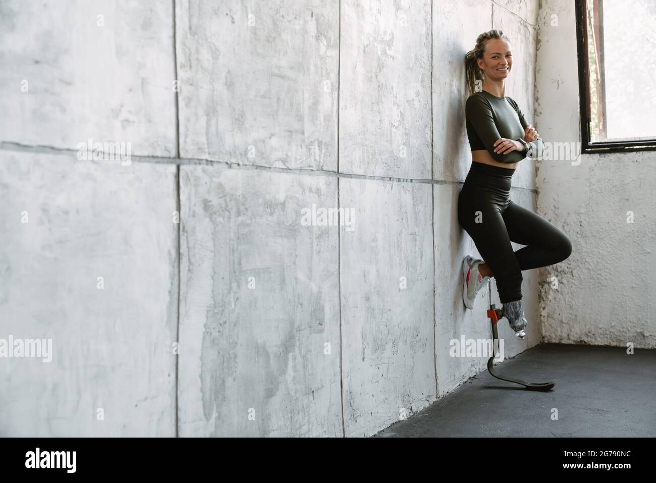 Giovane sportivo con protesi sorridente mentre si appoggia alla parete interna Foto Stock