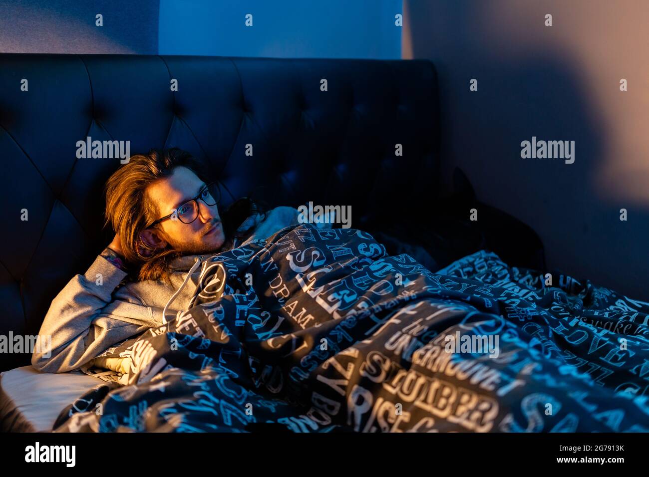 Un giovane uomo che si posa a letto guardando la TV prima di andare a dormire. Stile di vita, dopo il concetto oscuro Foto Stock