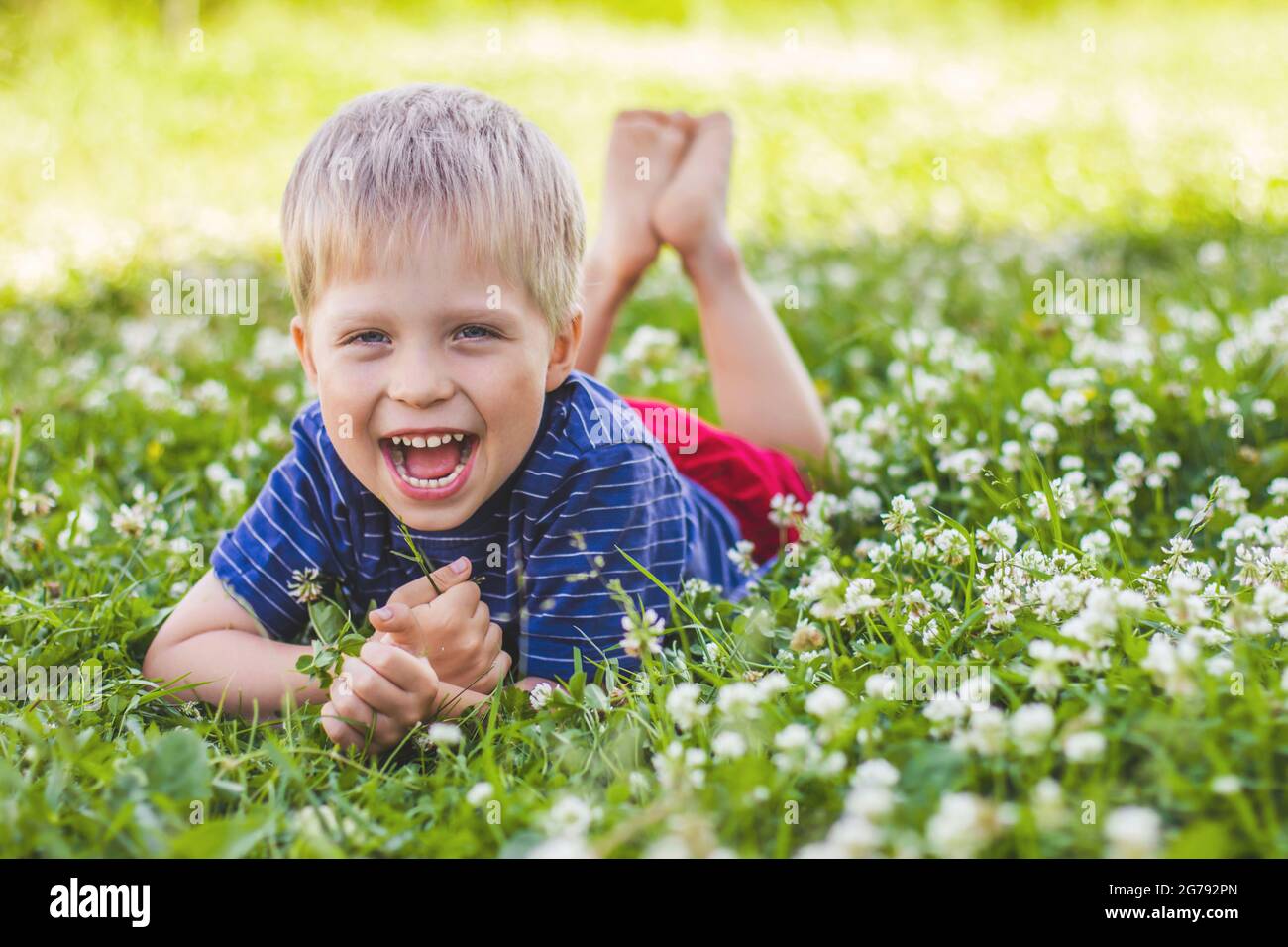 Un ragazzo felice e sorridente è sdraiato su un prato verde. Felice infanzia, estate e attività ricreative all'aperto Foto Stock