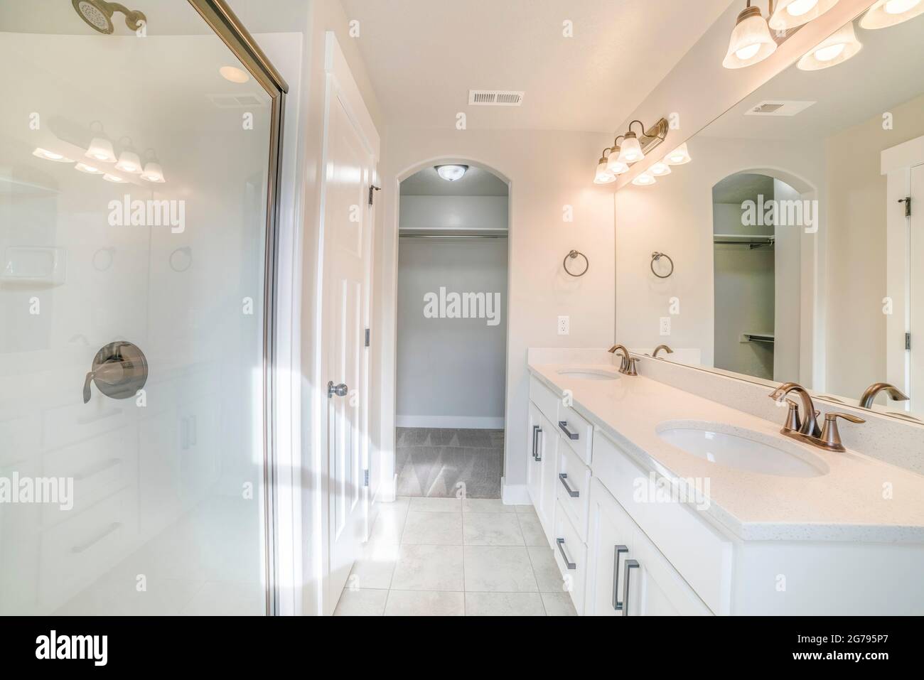 Interno di un bagno bianco con doccia con parete di vetro, lavabo e armadio vuoto Foto Stock