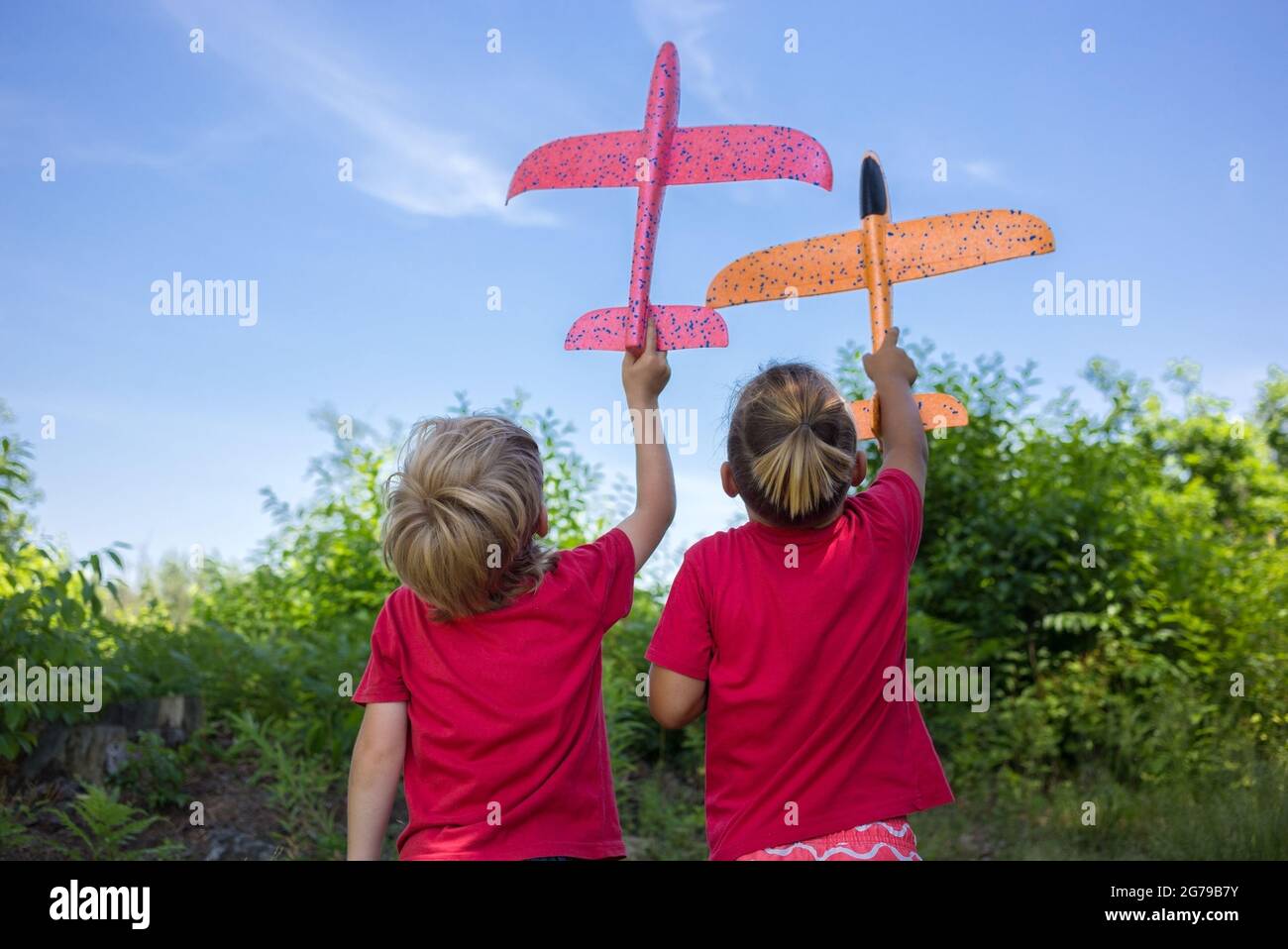 Due ragazzi in T-shirt rossa, si levano in piedi con le loro spalle, tenendo grandi aeroplani giocattolo in mani contro lo sfondo del cielo. Giochi, vita, sogni. Concetto di desi Foto Stock