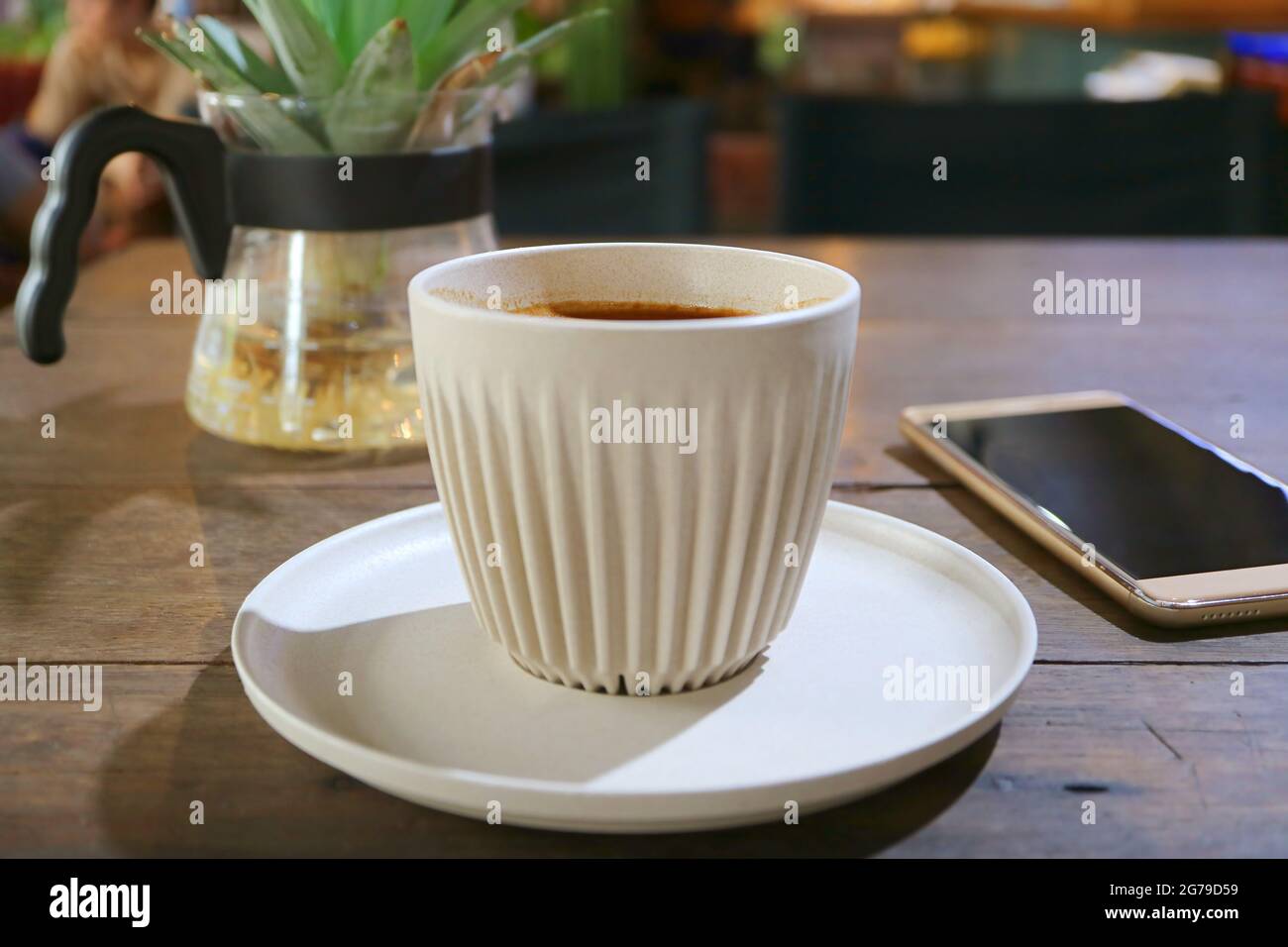 Tazza di caffè caldo su un tavolo di legno con schermo vuoto smartphone in background Foto Stock