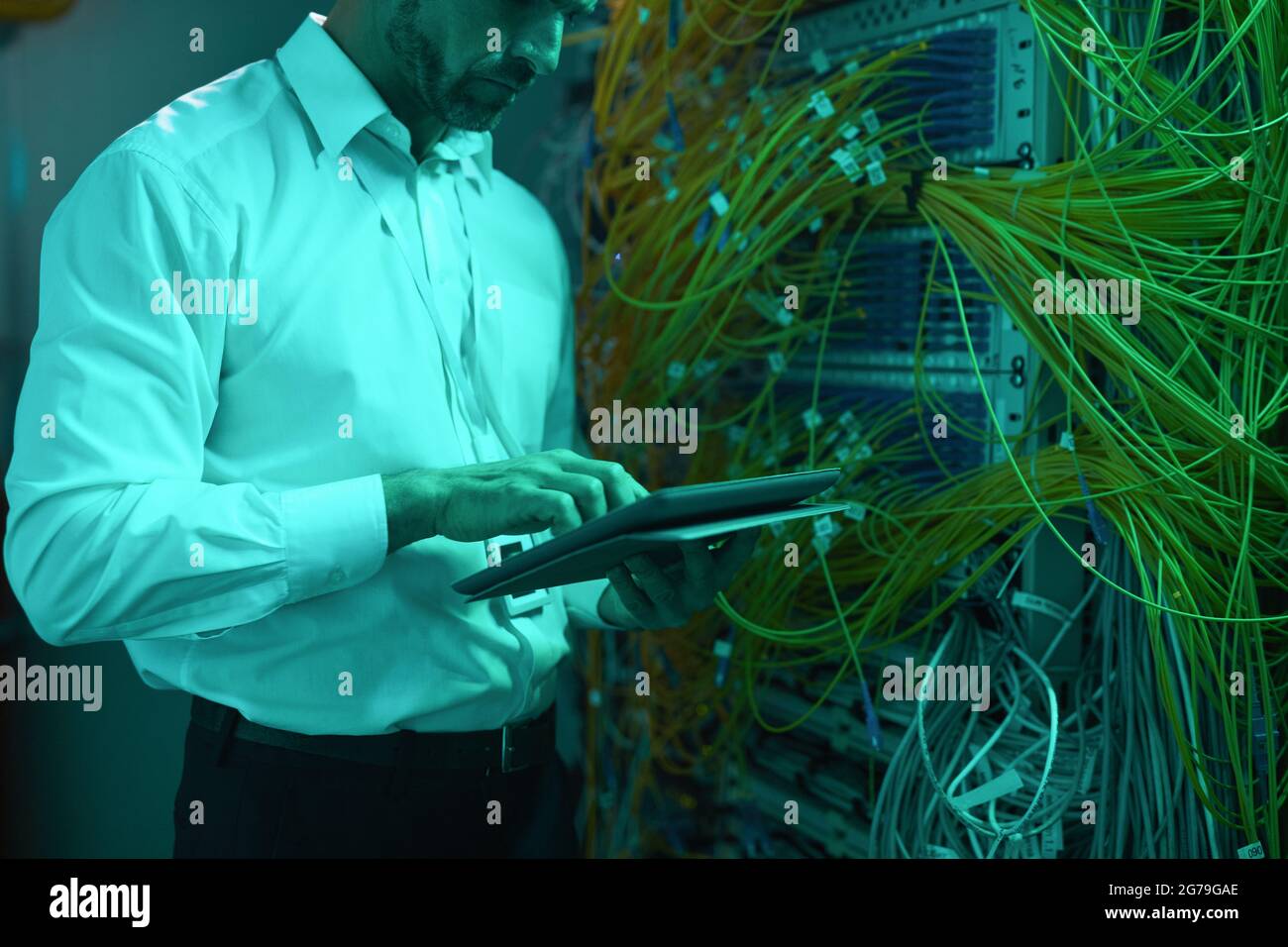 Ritratto ritagliato di un bel data engineer che utilizza un tablet digitale nella sala server mentre lavora con un supercomputer in luce blu, spazio di copia Foto Stock