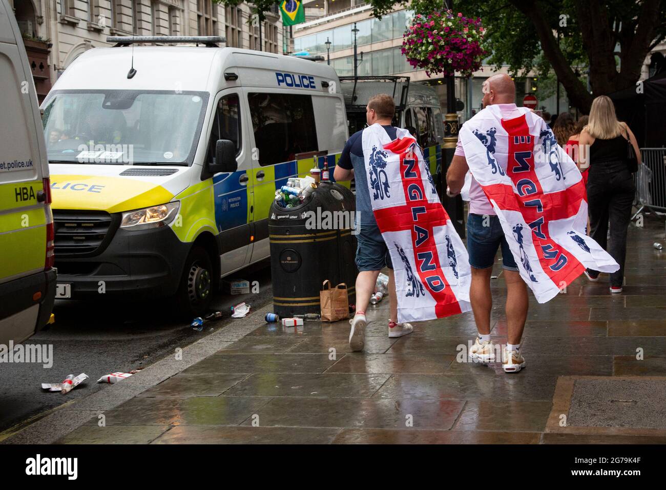 Due tifosi inglesi che indossano bandiere che passano furgoni di polizia vicino a Trafalgar Square nel centro di Londra prima della finale Euro 2020 Inghilterra contro Italia Foto Stock