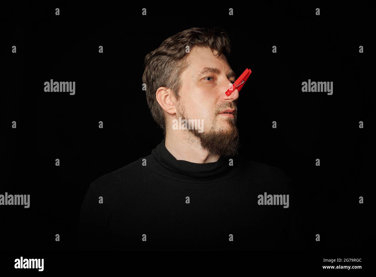 Uomo bearato con stendibiancheria sul naso. Malinconia, pupice divertente, concetto di scherzo. Ridere di te stesso. Stendibiancheria rossa - simbolo di auto-beffa e scherzare c Foto Stock