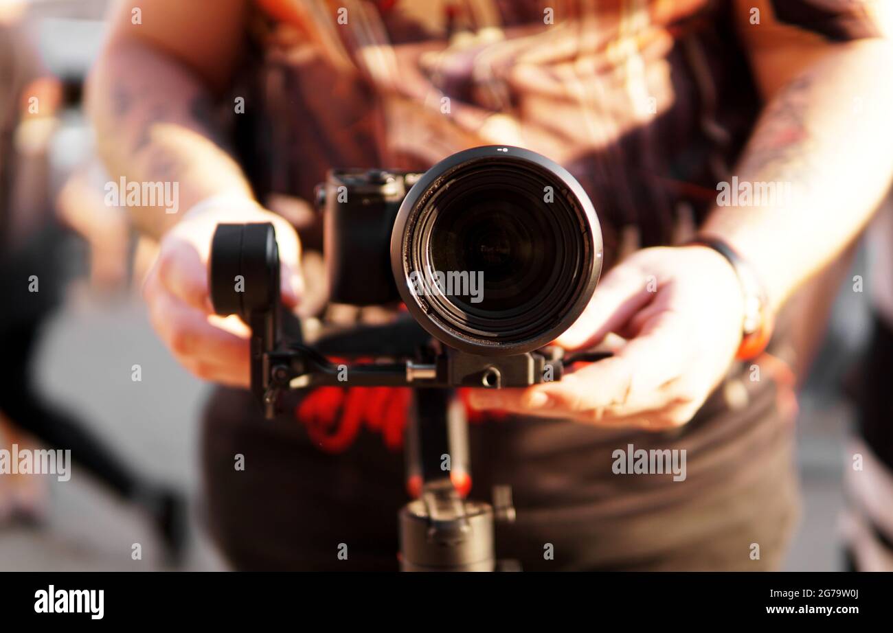 Un uomo con una macchina fotografica e un obiettivo. Fotocamera sullo stabilizzatore per riprese video. Sfondo sfocato e riflesso del sole Foto Stock