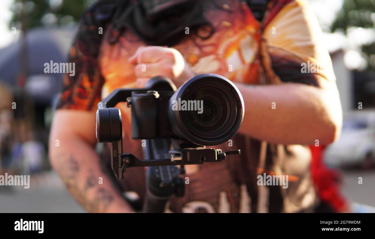 Un uomo con una macchina fotografica e un obiettivo. Fotocamera sullo stabilizzatore per riprese video. Sfondo sfocato e riflesso del sole Foto Stock