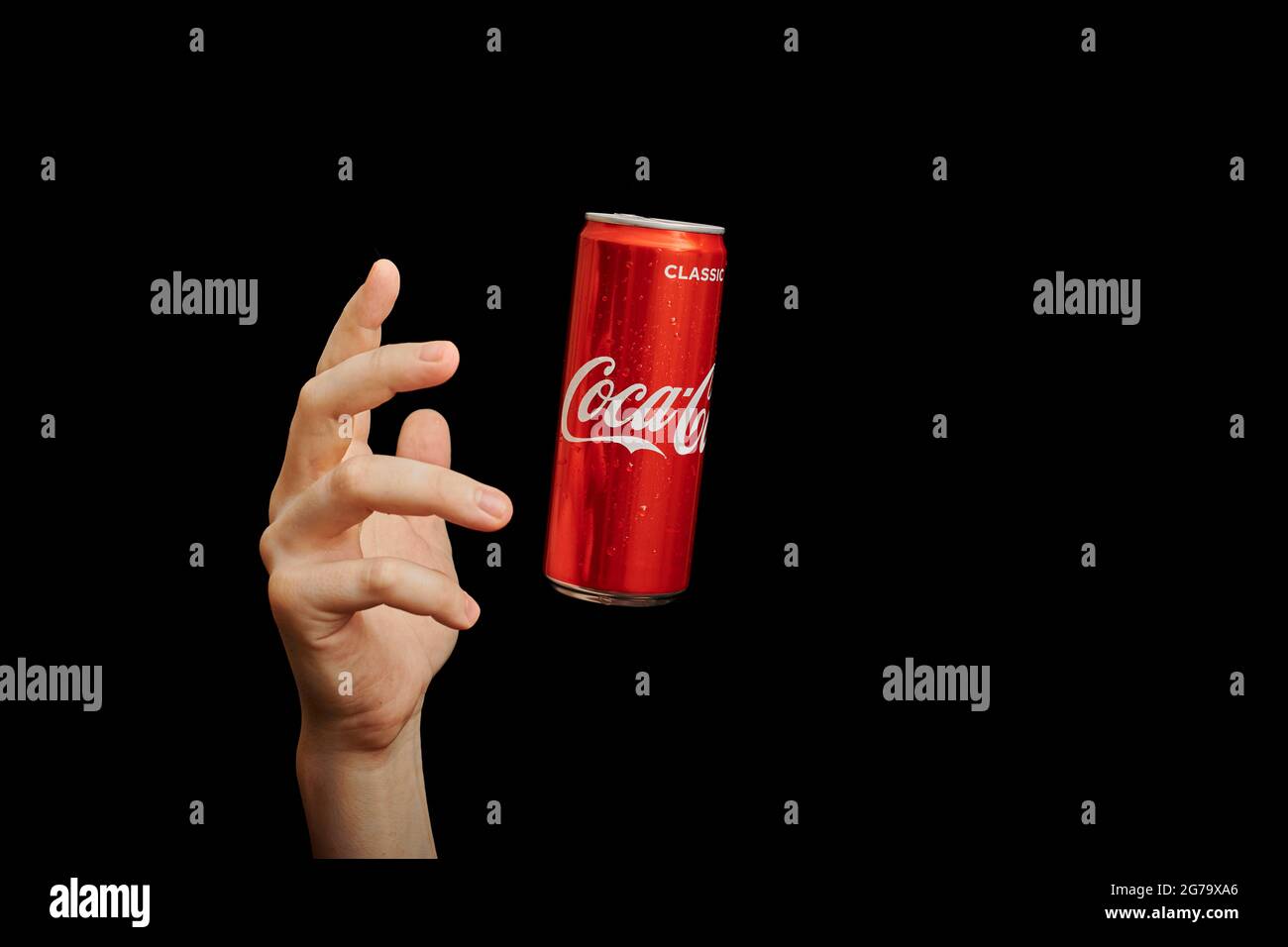 KALININGRAD, RUSSIA - 13 MARZO 2021 - la mano raggiunge la lattina di Coca Cola, sfondo nero. Classico vaso di coke, bevanda analcolica gassata. Prodotto dalla C Foto Stock