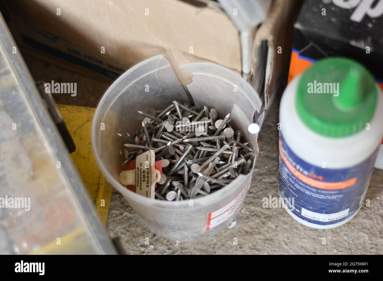 Una vasca di chiodi e una bottiglia di colla realizzata localmente su un cantiere Foto Stock