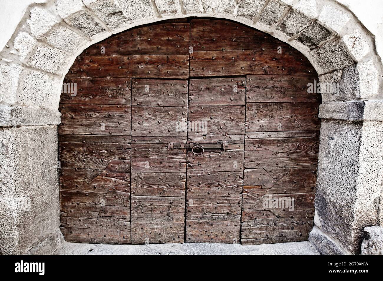 Ampia porta in legno a due ali, all'interno di una porta a due ali, incorniciata da un arco in pietra, la Lombardia Foto Stock