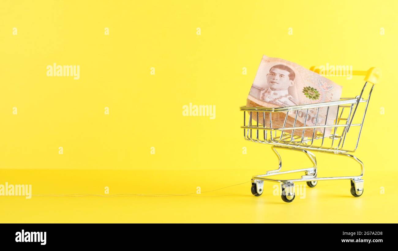 Carrello della spesa e mille note di baht thailandesi su uno sfondo giallo, primo piano. Acquisto del Black Friday e concetto di sconto Foto Stock