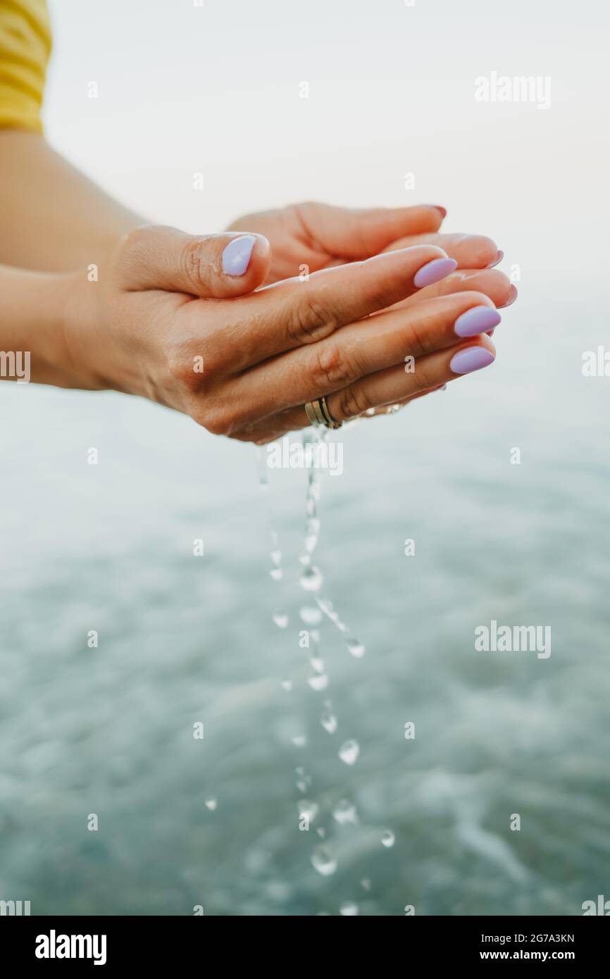 L'acqua che versa dalle mani del donna. Mare, vicino alle braccia femminili. Camicia gialla sullo sfondo. L'acqua è una forza vitale Foto Stock