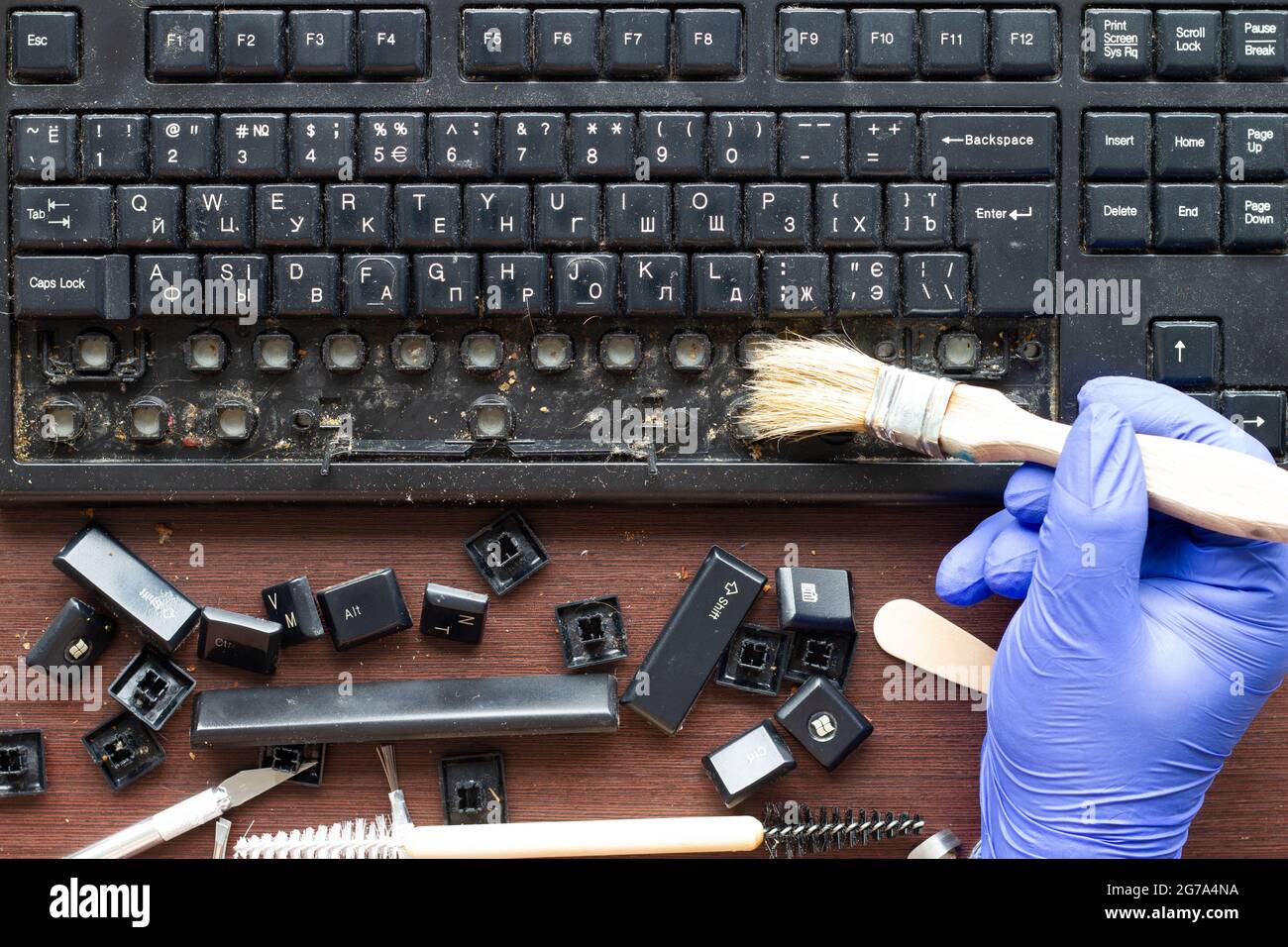 Un tecnico di elettronica professionale pulisce una tastiera del computer sporca con i tasti rimossi con una spazzola. Gli attrezzi per la riparazione e la pulizia Foto Stock