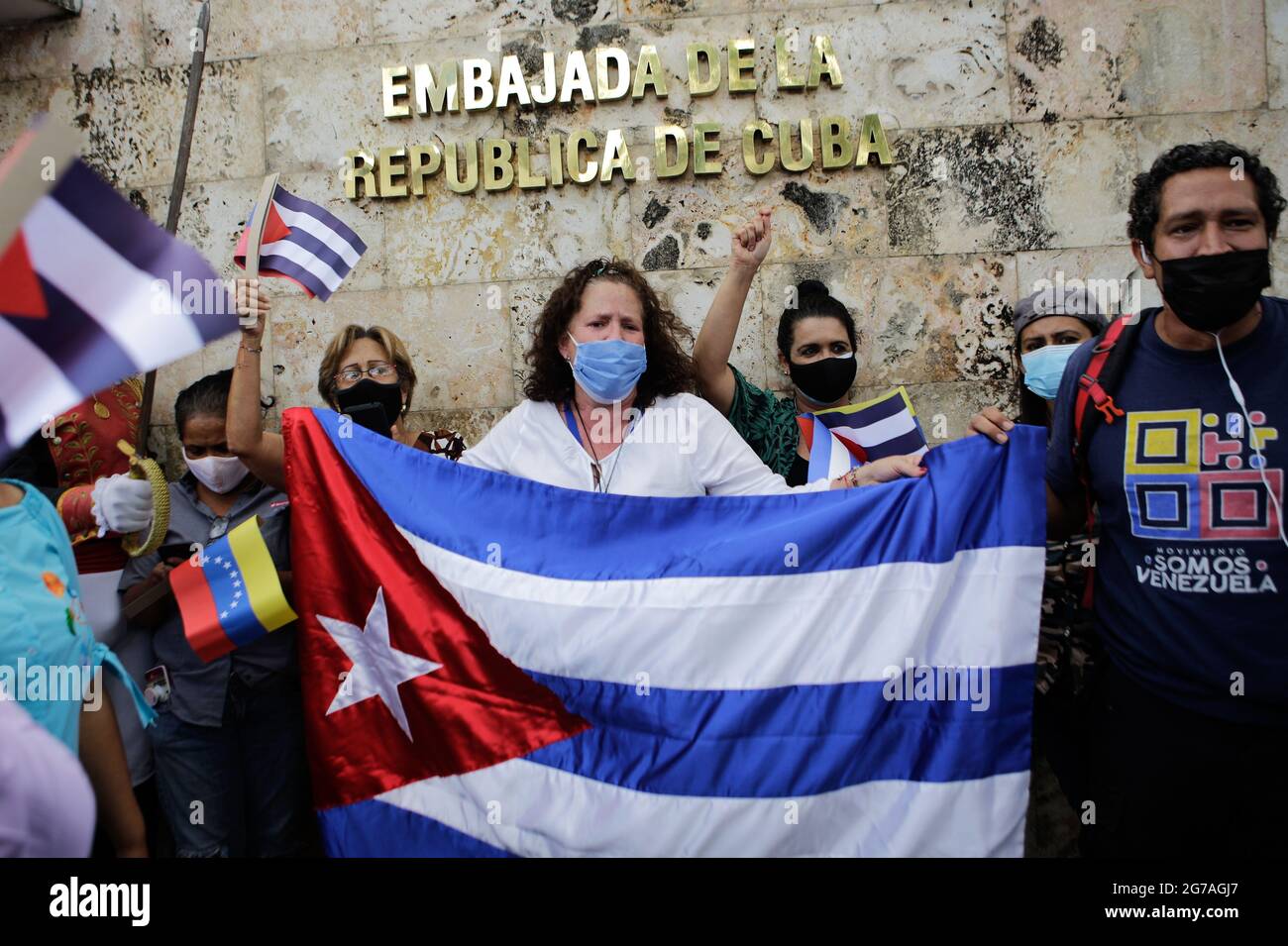 Caracas, Venezuela. 12 luglio 2021. I manifestanti che indossano copricendita hanno ondulato bandiere di Cuba durante un rally fuori dell'ambasciata cubana a sostegno del governo dell'isola. Decine di persone avevano dimostrato il giorno prima a l'Avana e in molte altre città cubane contro le carenze e l'oppressione. Gli osservatori hanno parlato delle più grandi manifestazioni di Cuba degli ultimi decenni. Credit: Jesus Vargas/dpa/Alamy Live News Foto Stock