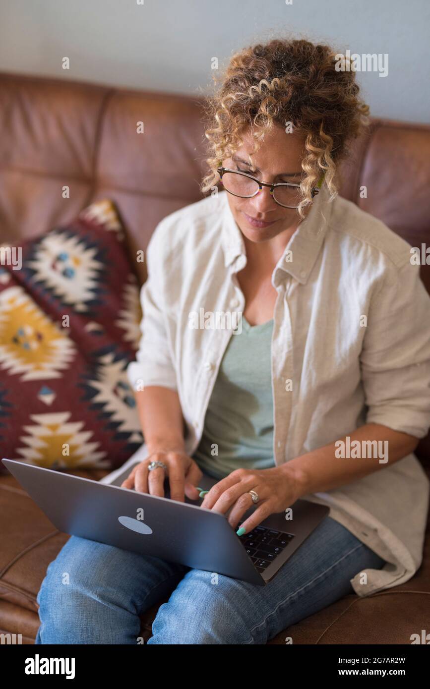 Giovane donna adulta siediti rilassati sul divano utilizzando il moderno computer portatile navigazione Internet wireless illimitato, giovani felici freelance lavoro sul computer digitando SMS da casa Foto Stock