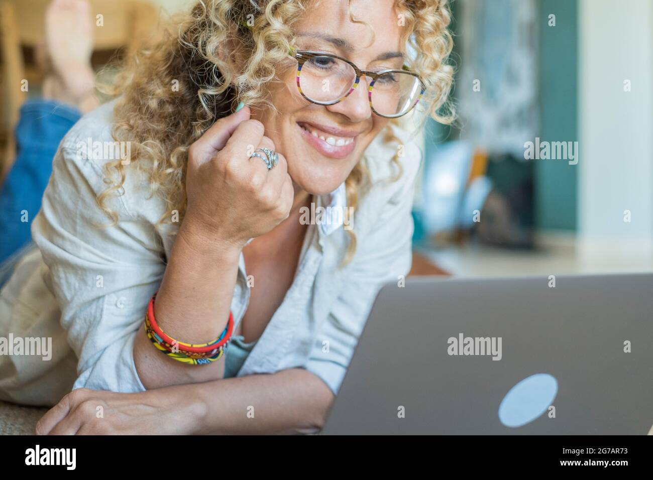 Felice donna singola si stese sul pavimento e lavorare con il computer portatile sorridente e divertendosi da sola a casa - concetto di persone e connessione internet online - giovane donna che guarda il computer rilassato sul pavimento Foto Stock