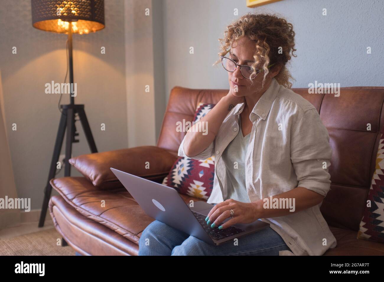 Persone connesse a Internet navigare in rete. Donna giovane premurosa negli occhiali che usa il computer mentre si siede sul divano a casa - relax indoor con computer portatile da solo Foto Stock