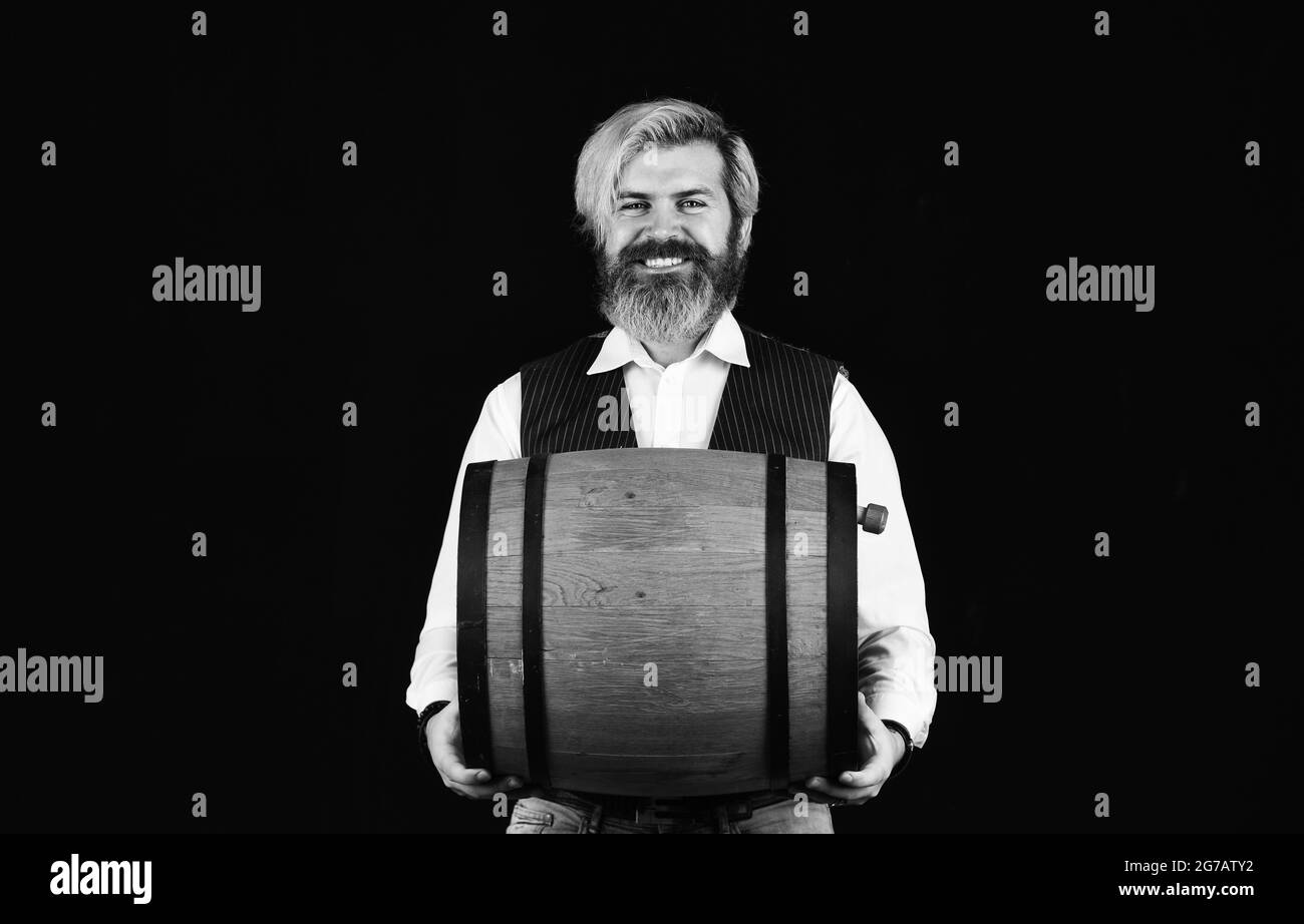 Concetto di cantina. Produzione di tradizione enologica familiare. L'uomo ha bearato hipster barile di legno per vino sfondo nero. Vino fatto in casa. Prodotto di fermentazione Foto Stock