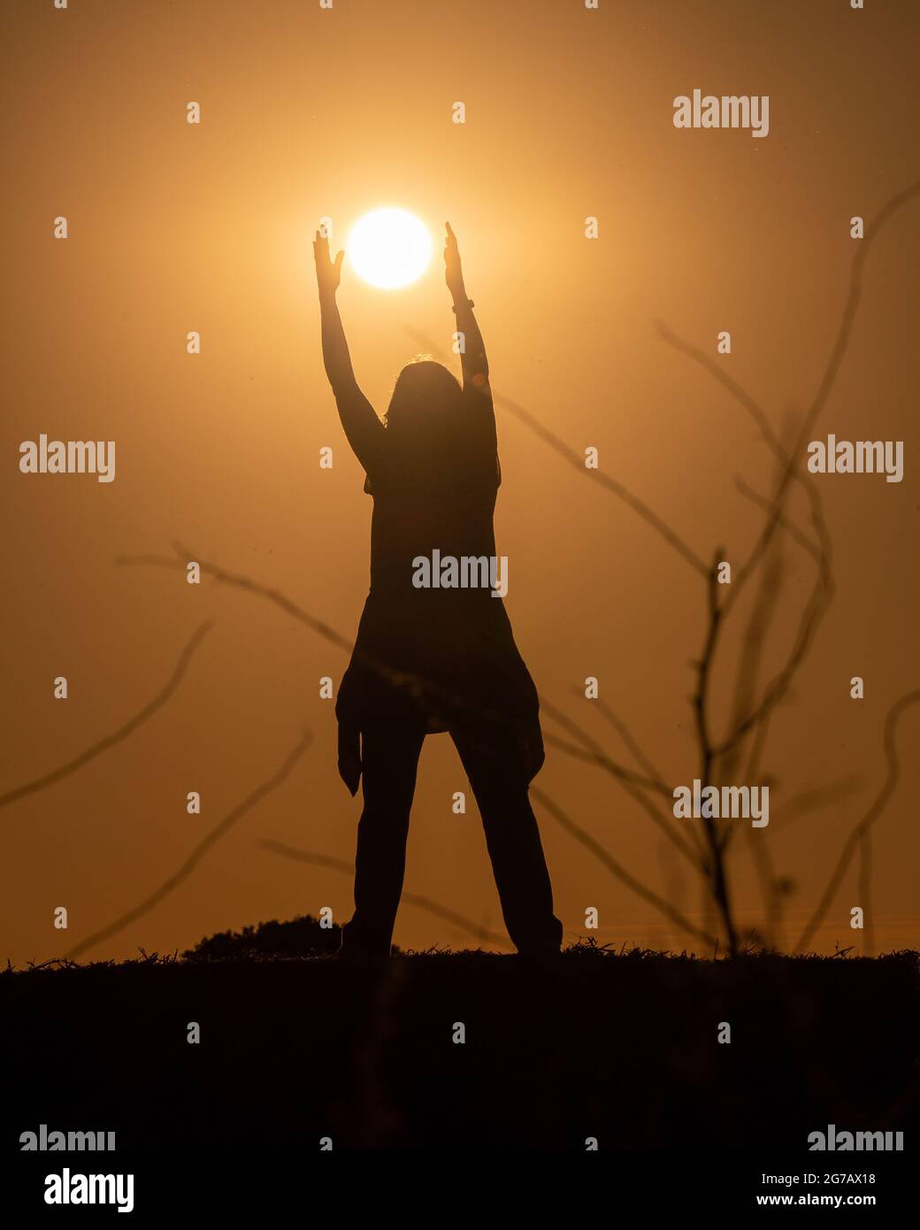 Silhouette di una donna in campagna cercando di prendere il sole al tramonto. Contrasto nero con arancio dorato. Immagine verticale. Foto Stock