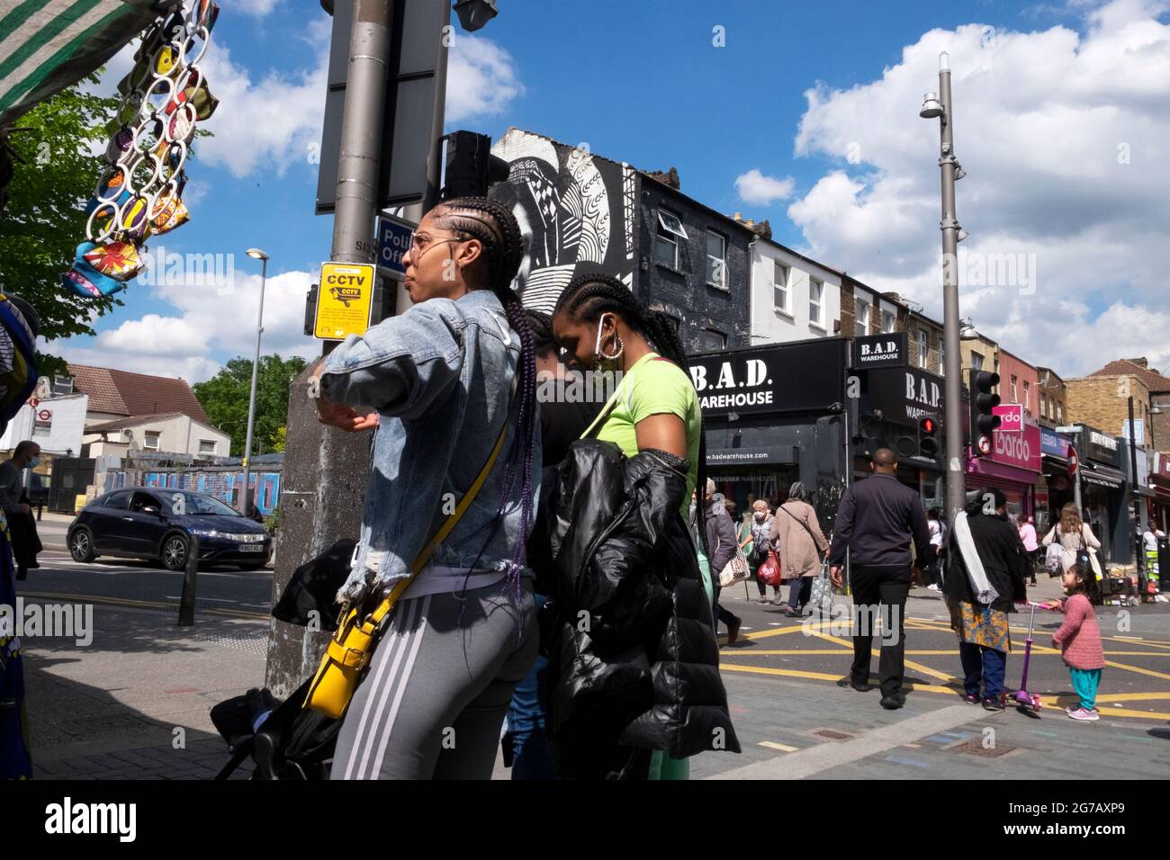 Giovani donne nere che fanno shopping al mercato di strada e persone che attraversano la strada in estate su Walthamstow High Street Londra E17 Regno Unito KATHY DEWITT Foto Stock