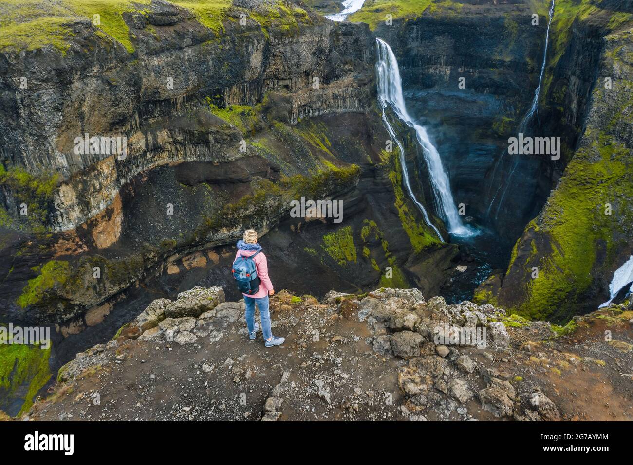 Vista aerea di una donna con zaino che si gode l'altopiano islandese e la cascata Granni. Islanda Foto Stock