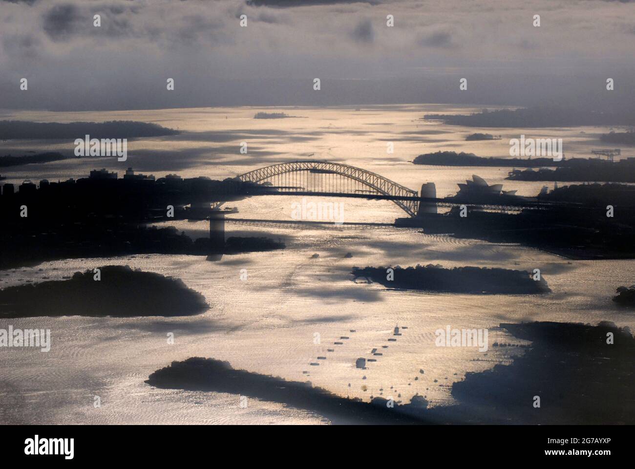 Immagine attraverso una finestra dell'aereo che mostra il porto di Sydney, il ponte e l'Opera House, con sagome contro la luce. Sydney, Australia Foto Stock