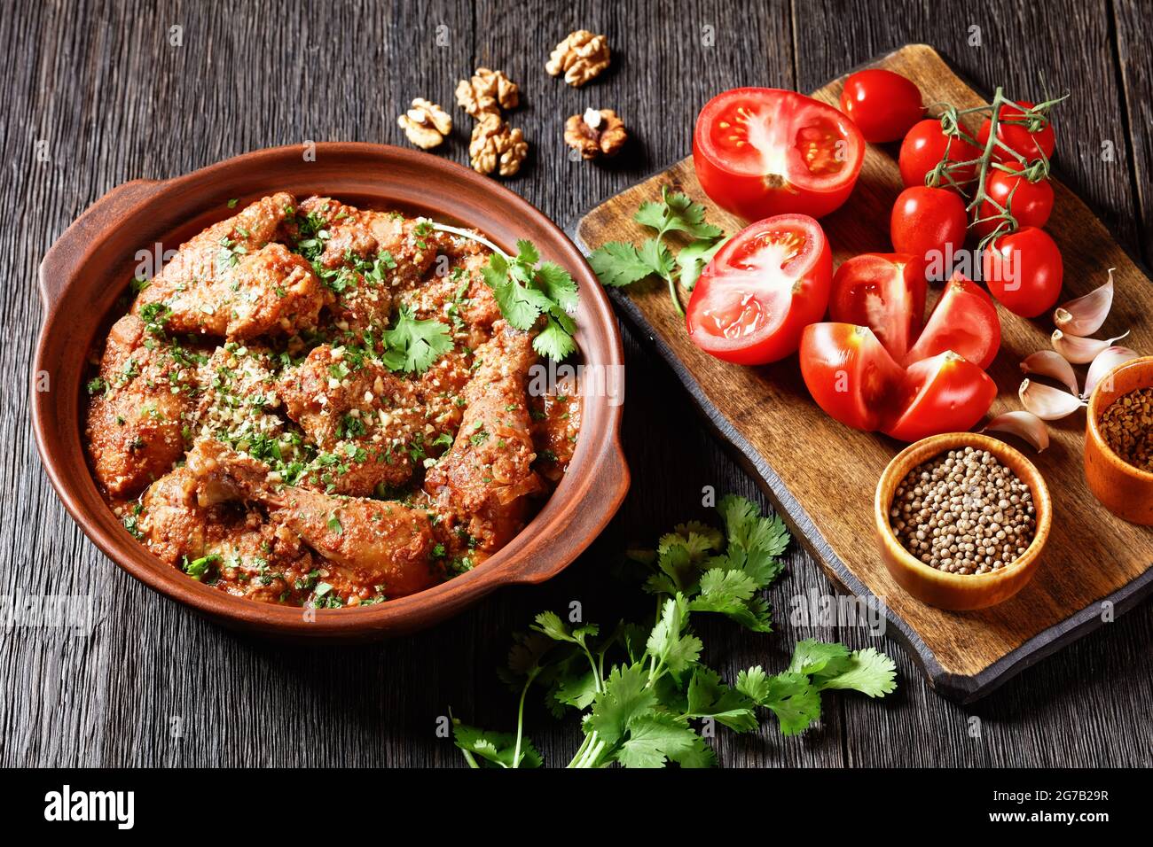 Chakhokhbili, pollo stufato, pomodoro con erbe fresche, noci e spezie in una pentola di argilla su un tavolo di legno con ingredienti su un tagliere, georgia Foto Stock