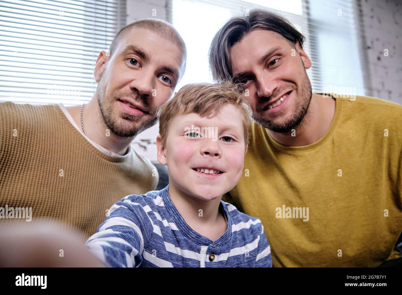 Positivo presteen ragazzo prendendo selfie con i suoi due padri sorridenti per postare dei social media Foto Stock