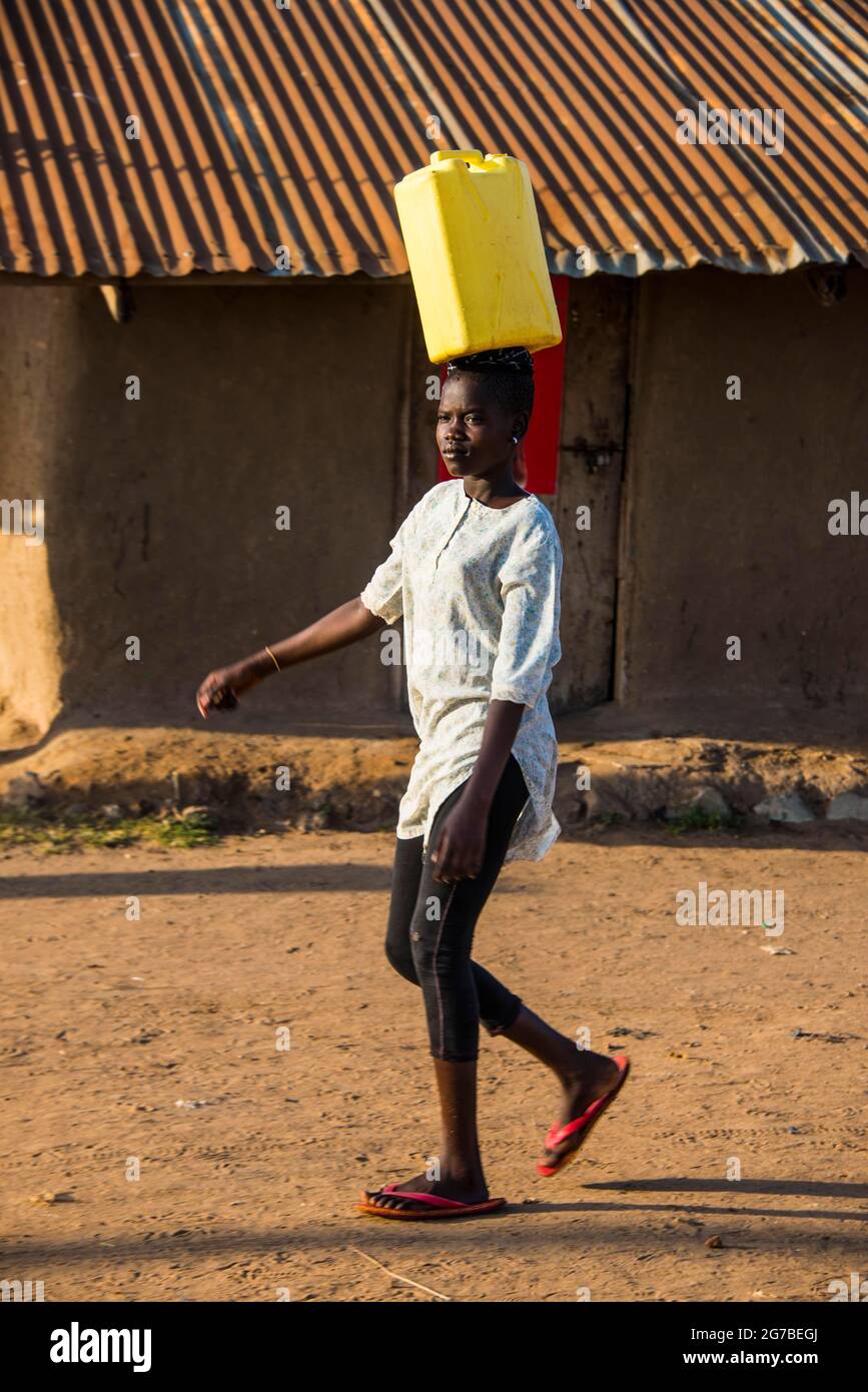 La donna che porta un barattolo di acqua sulla sua testa portando acqua home dal lago Albert, Uganda, Africa Foto Stock