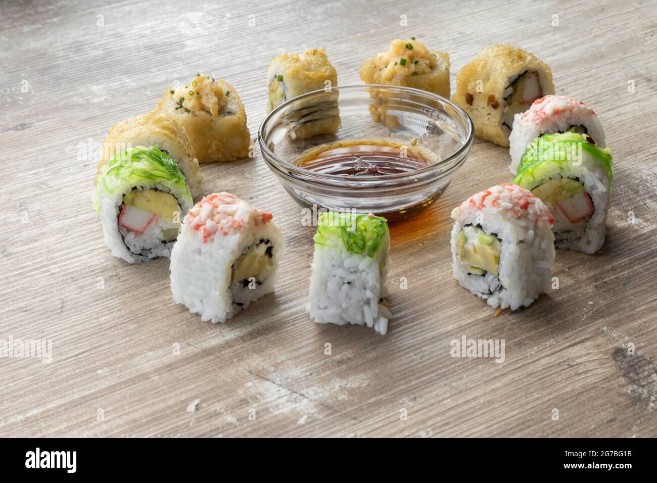 su un tavolo di legno testurizzato sushi rotola a forma di cerchio intorno ad una ciotola con salsa di soia, cibo e stile di vita sano, studio Foto Stock