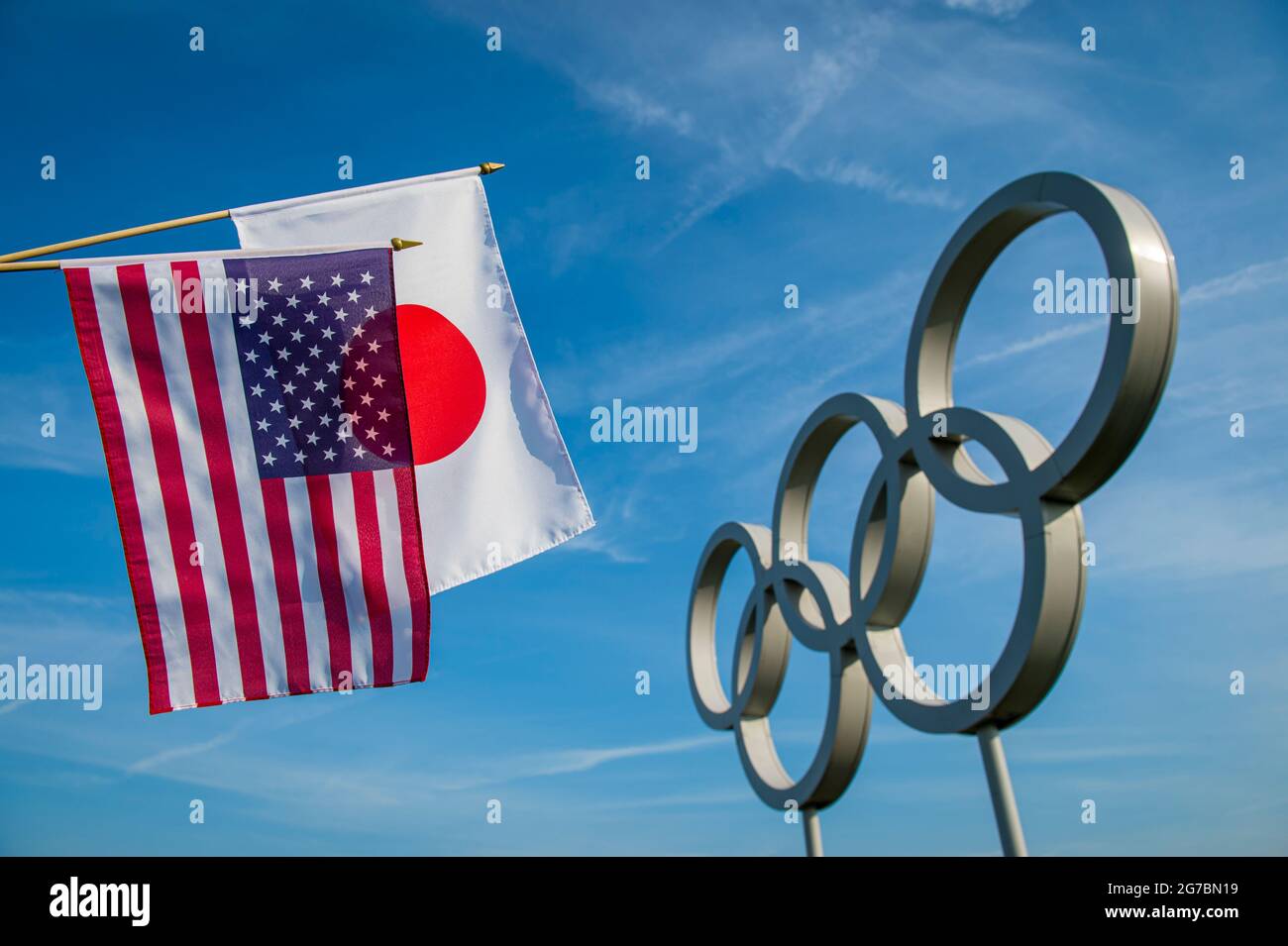 RIO DE JANEIRO - MARZO 2016: Bandiere giapponesi e americane appendono insieme davanti a un grande set di brillanti anelli olimpici metallici sotto il cielo azzurro. Foto Stock