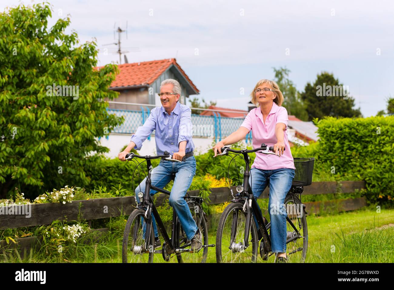 Senior l uomo e la donna che esercitano con le biciclette all'aperto sono un giovane Foto Stock