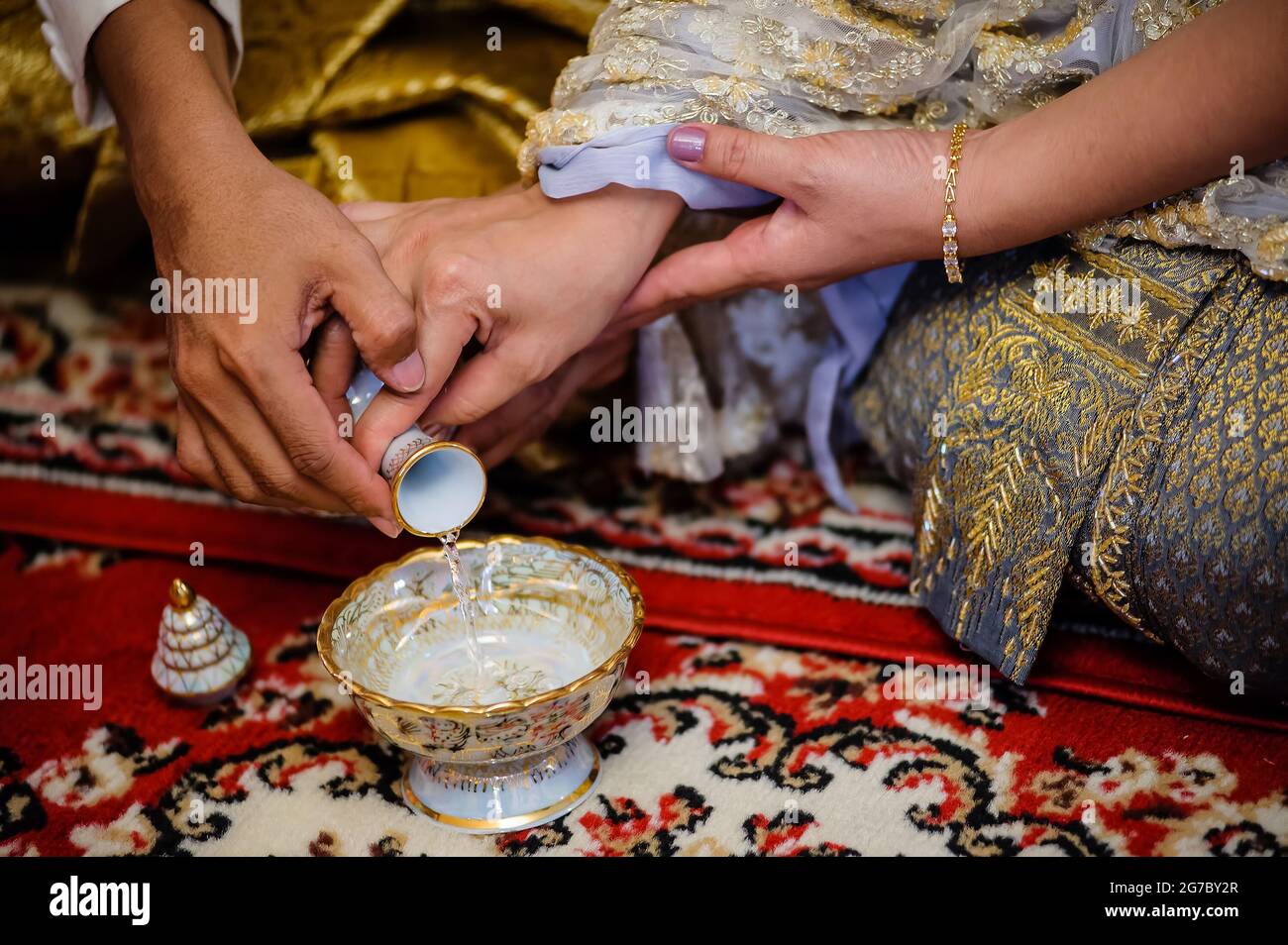 Le mani della sposa e dello sposo versano insieme acqua Santa durante il matrimonio tradizionale in stile thailandese Foto Stock