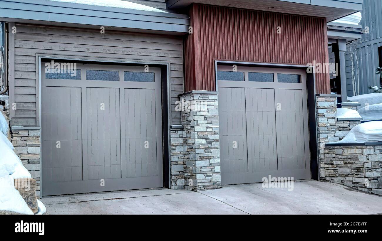 Pano due garage auto con porte in vetro grigio panato alla facciata di casa in inverno Foto Stock
