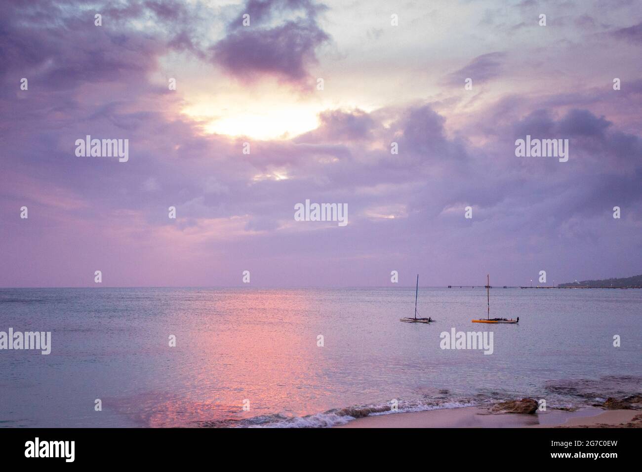 Due barche a vela ormeggiate nei Caraibi al largo della riva vicino Frederiksted, St Croix, USVI come il tramonto si riflette nelle nuvole e il mare. Foto Stock