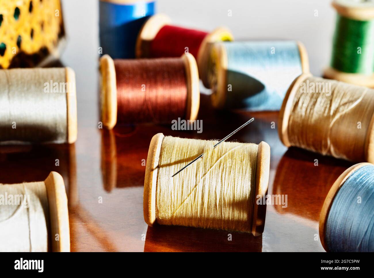 Bobine di filo colorato e ago su tavola di legno, nel cestello di cucitura di fondo Foto Stock