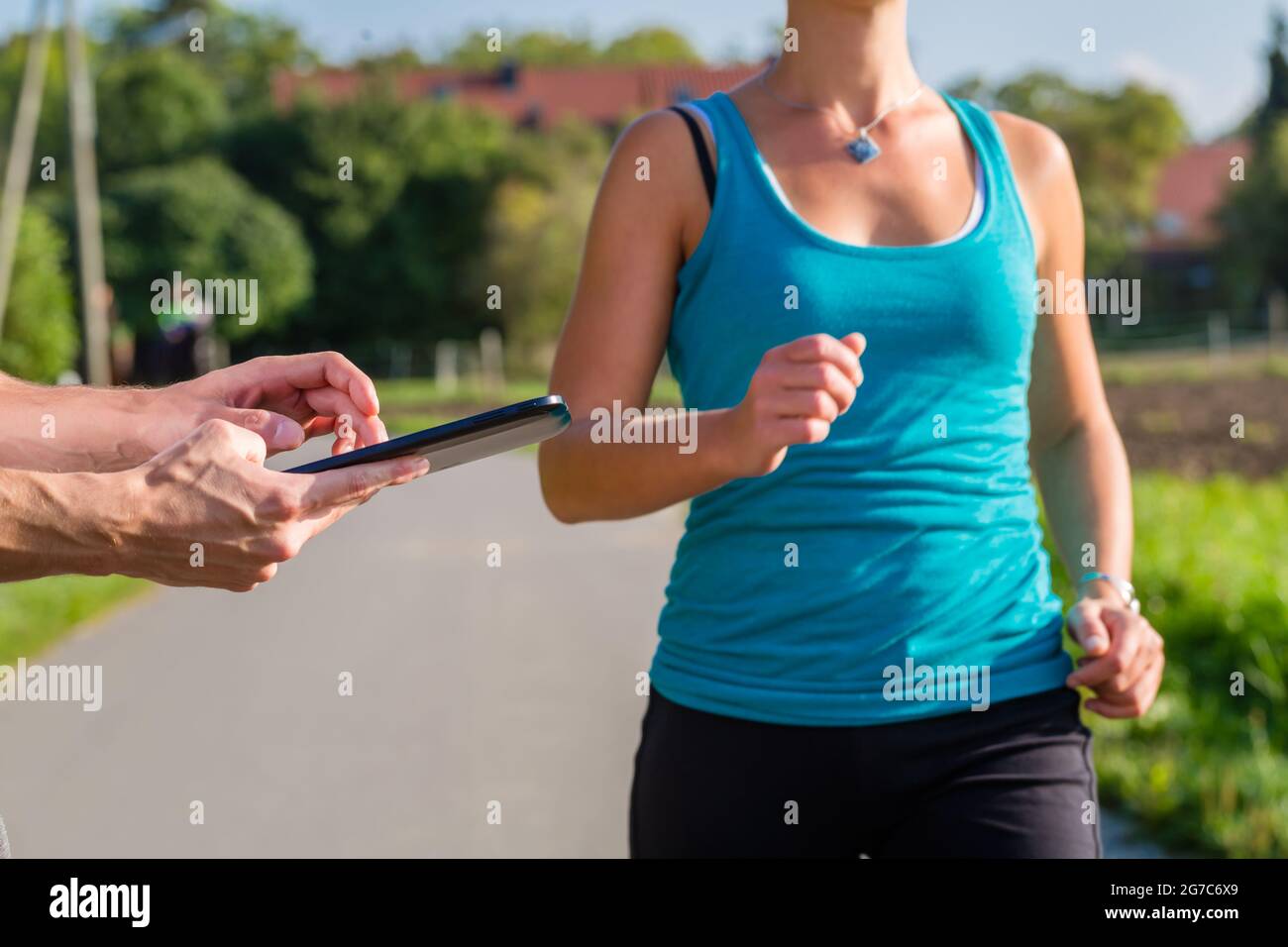 Donna facendo jogging o in esecuzione outdoor sport per il fitness su strada rurale, il trainer arrestando il suo tempo con app sul computer tablet Foto Stock