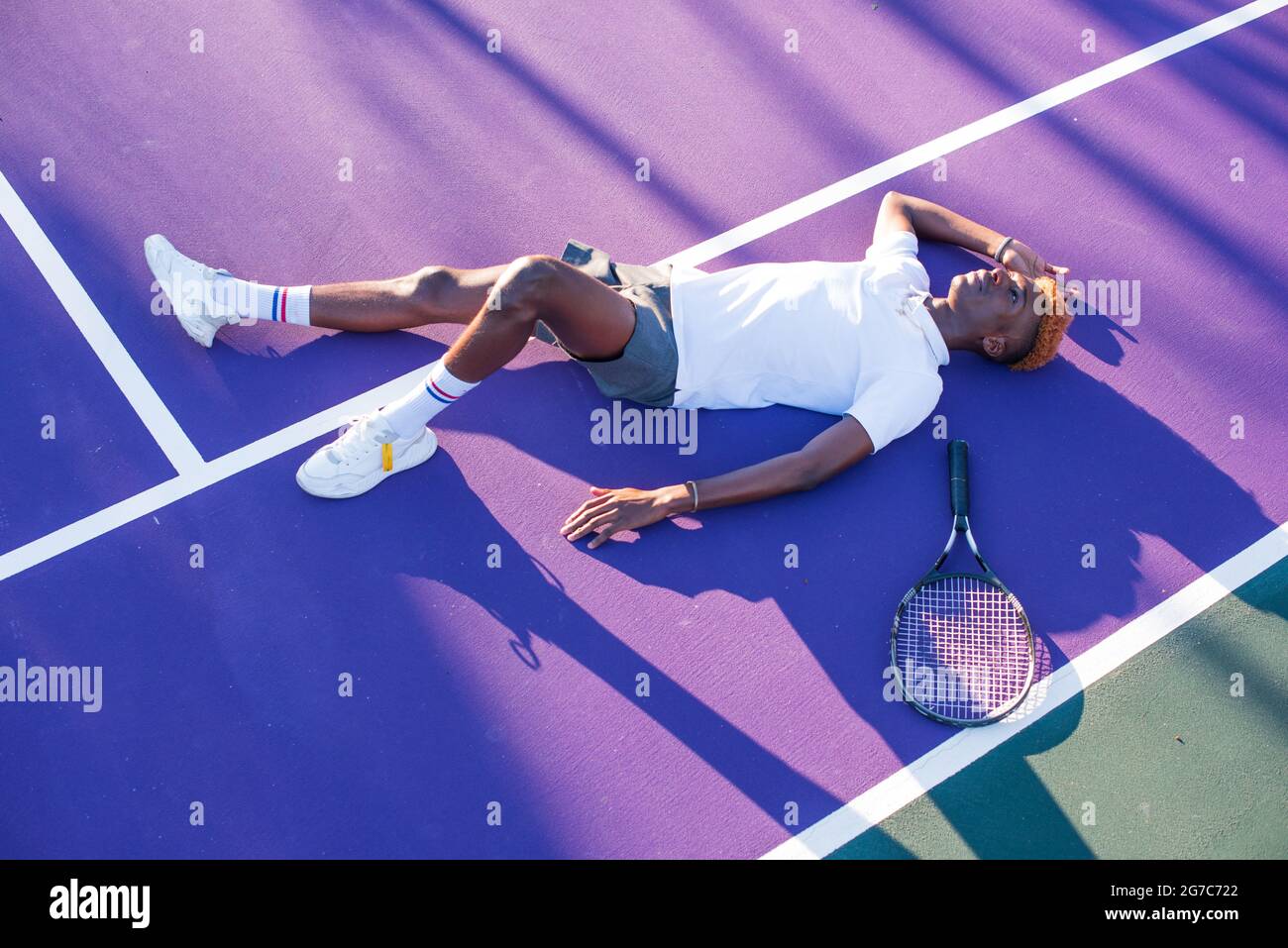 Giovane uomo adagiato su un campo da tennis di colore viola Foto Stock