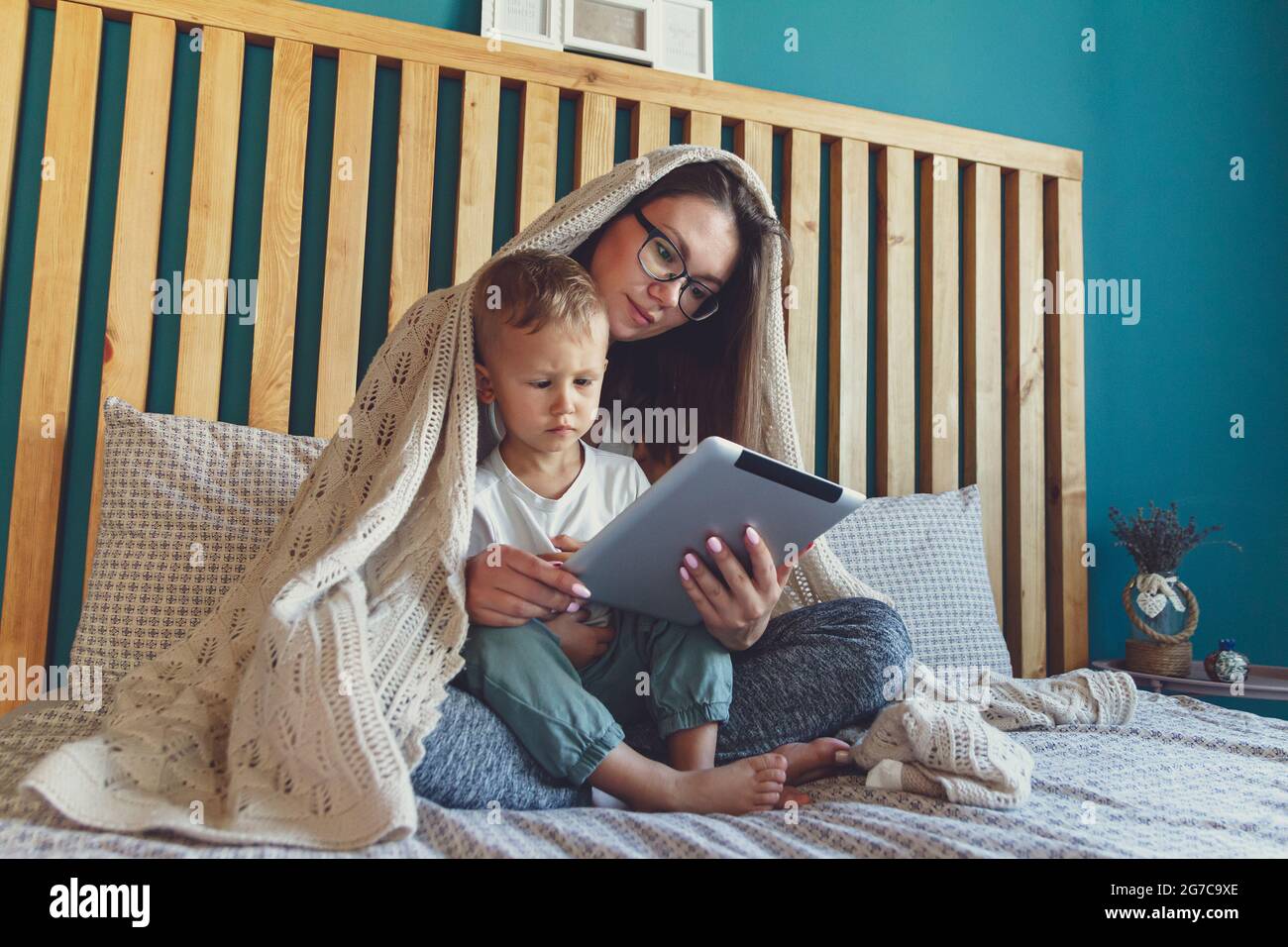 Mamma e figlio giovani con una tavoletta sotto una coperta accogliente nel letto Foto Stock
