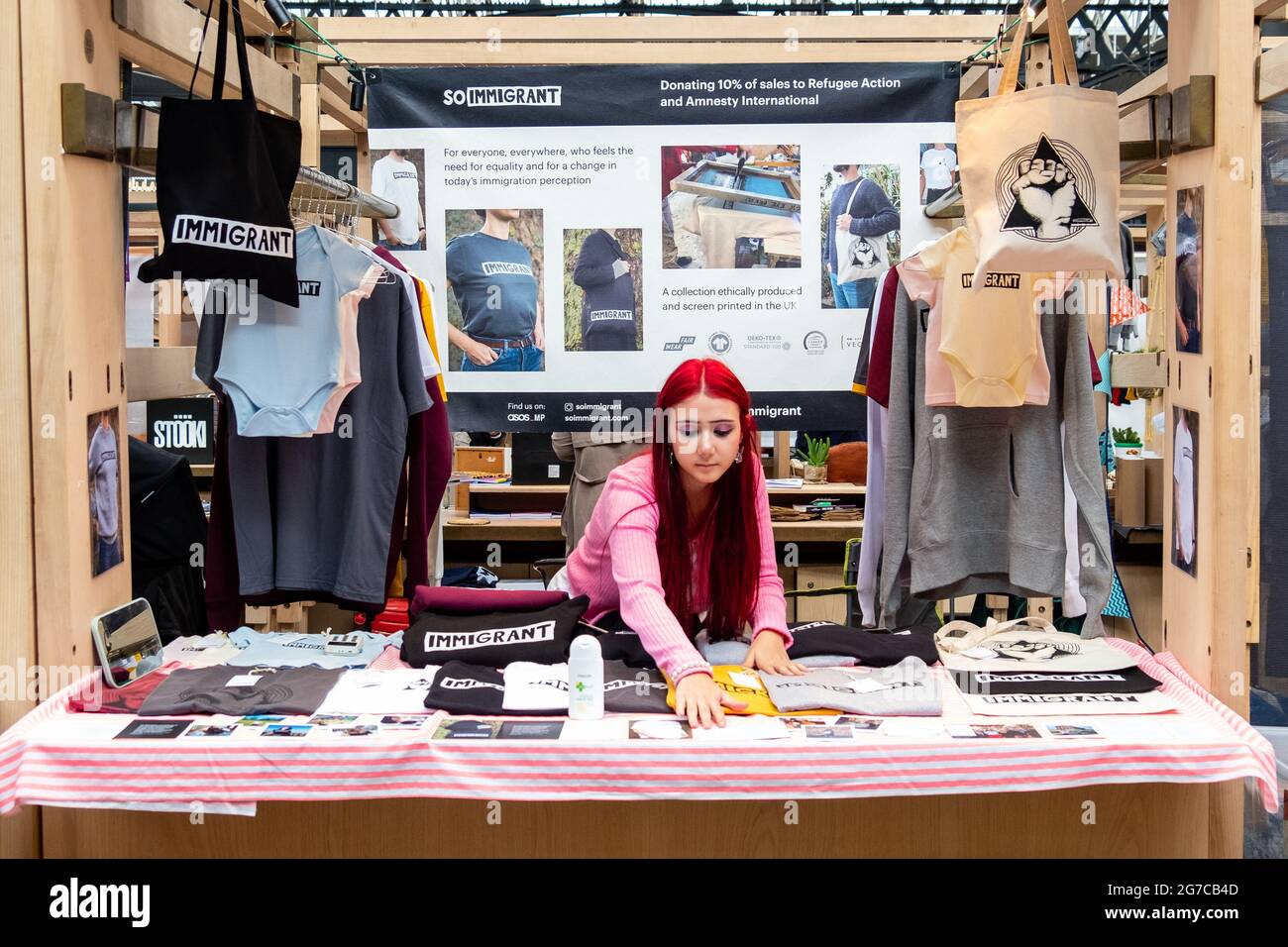 Londra- Luglio 2021: Una ragazza che vende una linea di articoli di moda al mercato Spitalfields a Londra Est con la parola / branding ‘immigrante’ Foto Stock