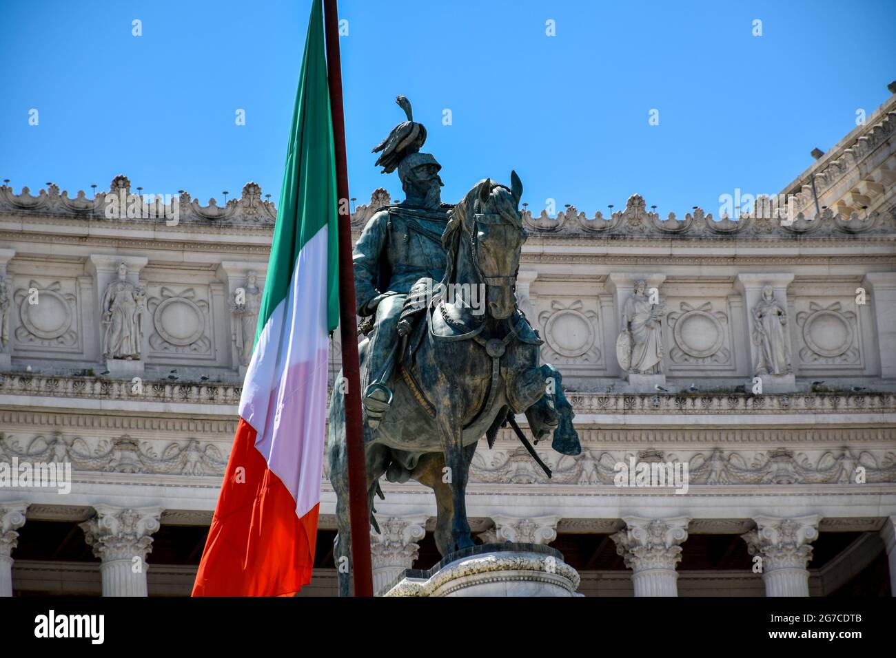 Una grande bandiera nazionale italiana accanto alla statua equestre del Re Vittorio Emanuele II nel centro di Roma Foto Stock