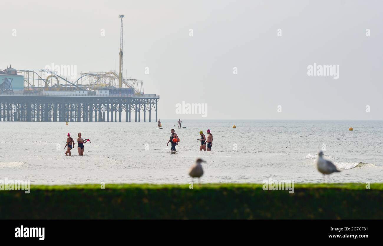 Brighton UK 13 luglio 2021 - i nuotatori e i paddle boarder del mattino presto godono della bassa marea e del sole fuori della spiaggia di Brighton come tempo caldo è previsto per arrivare nei prossimi giorni in Gran Bretagna con le temperature previste per raggiungere gli alti 20 entro il fine settimana : Credit Simon Dack / Alamy Live News Foto Stock