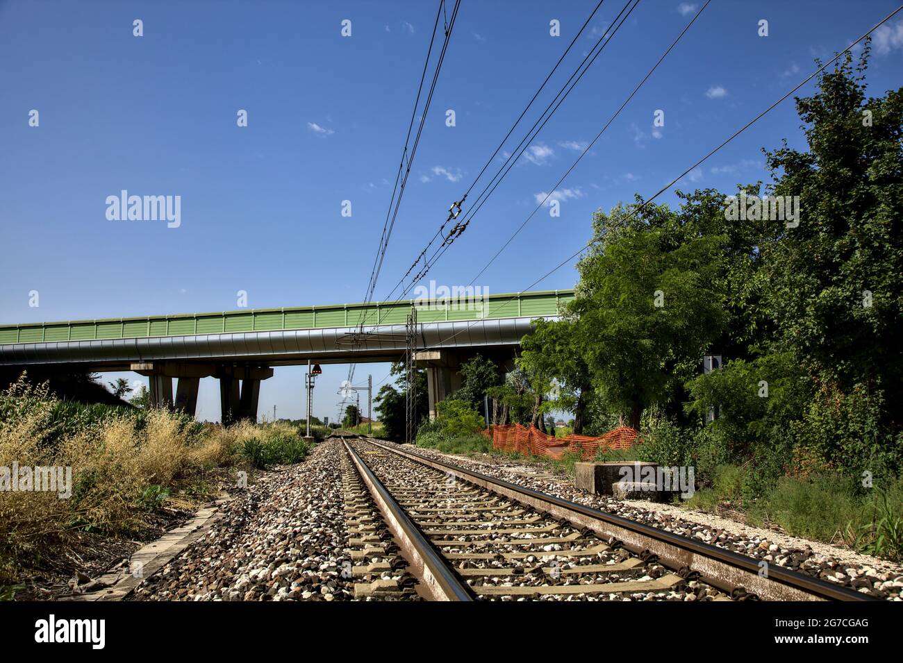 La ferrovia passa sotto un viadotto nella campagna italiana in estate Foto Stock