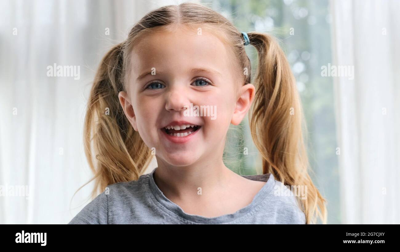 Ritratto di un bambino con gli occhi blu ride con un sorriso togoteo. Divertente bambina sorridente guardando la macchina fotografica a casa. Carino bambino di 3 anni preschool chi Foto Stock