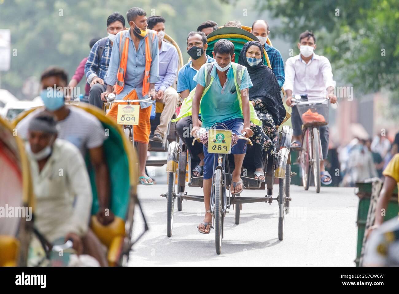 Persone che camminano o cavalcano risciò sul loro modo di lavorare nella corsa mattutina a Dhaka martedì 12 luglio. Il Bangladesh sta attraversando un'impennata di COVID-19, con un record di 13768 casi lunedì 12 luglio. Il 14 luglio, le restrizioni di blocco saranno attenuate per nove giorni per le celebrazioni Eid-ul-Azha. Foto Stock