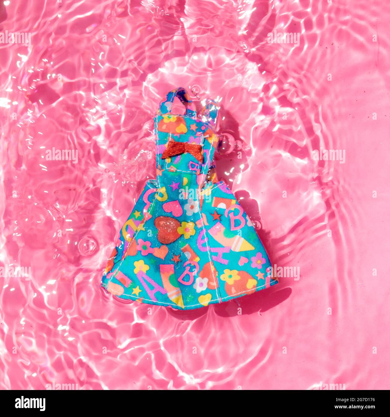 Abito colorato e leggero che galleggia in acqua su sfondo rosa pastello alla moda. Sotto il sole estivo luminoso. Concetto minimo di vacanza estiva e tendenze moda. Foto Stock