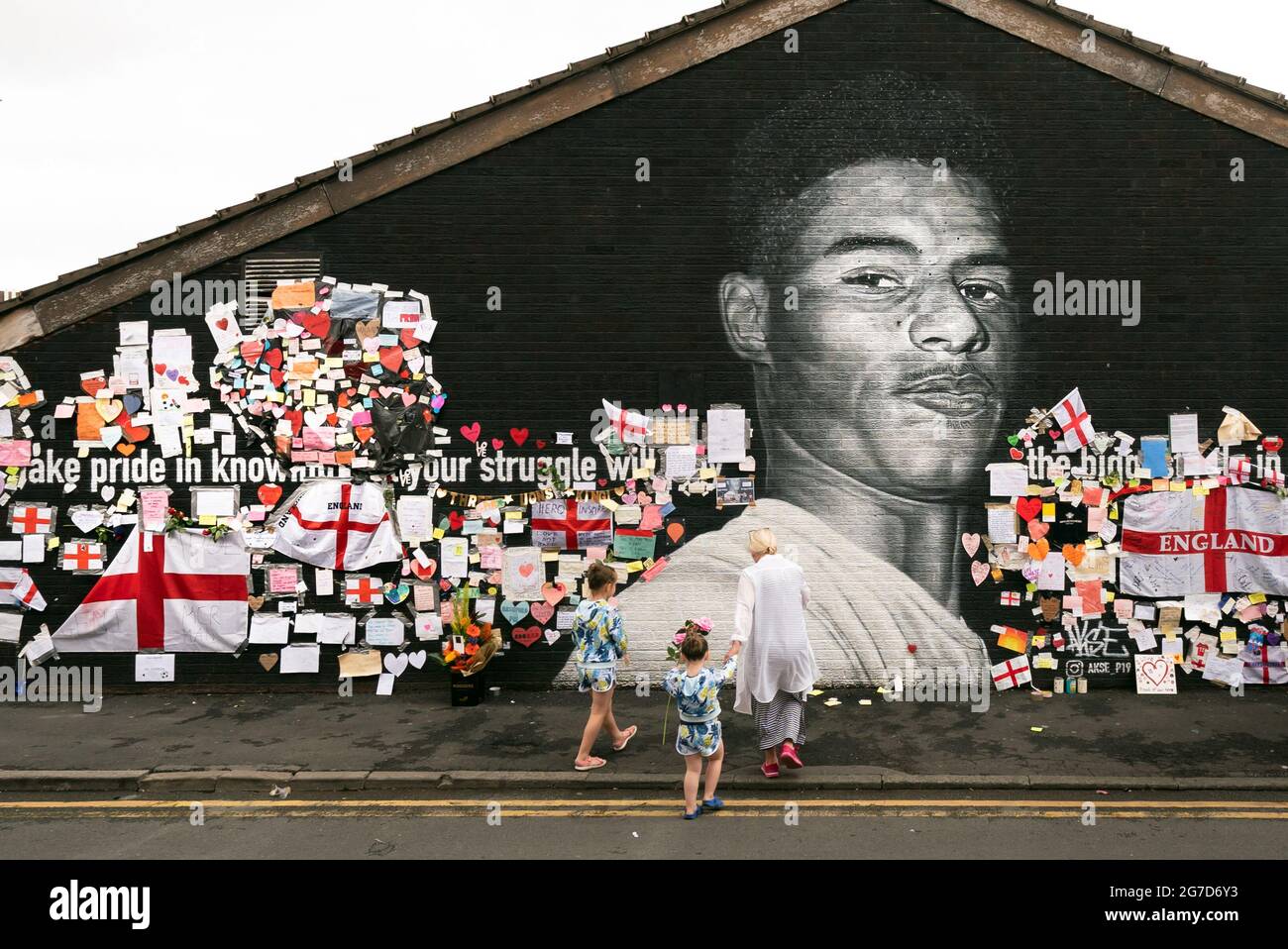 Marcella Jepson-Jones, sette anni, con la sorella Dolly Jepson-Jones e la nonna Lynda Swire lasciano le rose a un murale dell'attaccante del Manchester United e del giocatore d'Inghilterra Marcus Rashford sul muro del Coffee House Cafe su Copson Street, Withington, Che è stato vandalizzato dopo che la squadra di calcio inglese ha perso la finale UEFA Euro 2021. Data immagine: Martedì 13 luglio 2021. Foto Stock