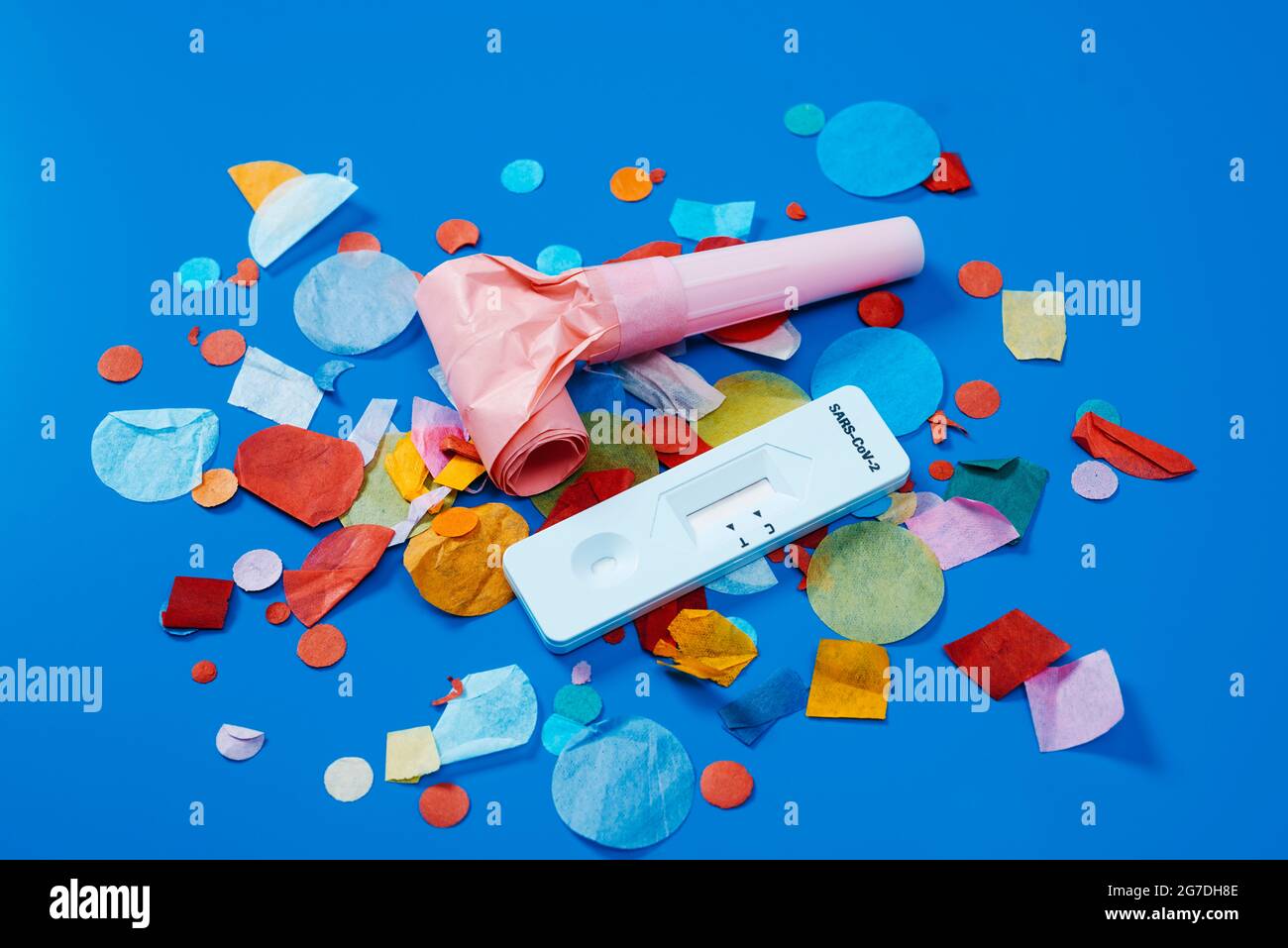 un dispositivo di test diagnostico dell'antigene covid-19, un corno rosa e alcuni confetti multicolori su sfondo blu, come un set di festa sicuro Foto Stock