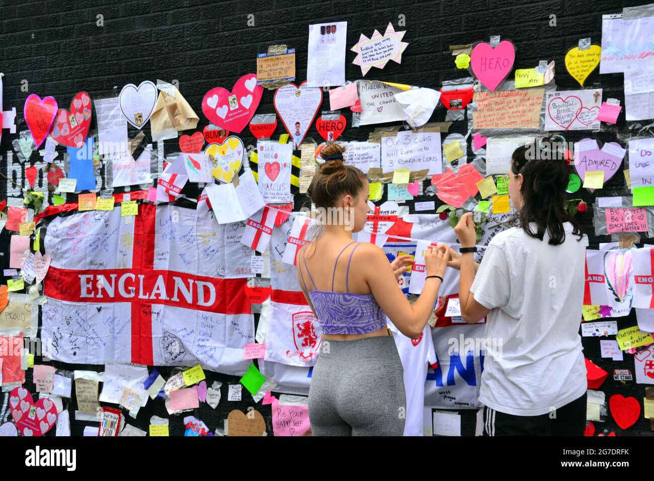 La gente lascia fiori e centinaia di note di supporto, immagini, bandiere e messaggi anti-razzisti sul gigante giocatore britannico di Manchester Marcus Rashford murale a Withington, Manchester, Inghilterra, Regno Unito, che è stato vandalizzato con graffiti abusivi dopo la perdita di calcio in Inghilterra Euro2020 l'11 luglio 2021. Il murale è stato creato dall'artista di strada francese Akse P19 sulla parete del Coffee House Cafe in Copson Street. Marcus Rashford è un calciatore del Manchester United. Akse riparò completamente il murale danneggiato entro il 13 luglio 2021. Data immagine: 13 luglio 2021. Foto Stock
